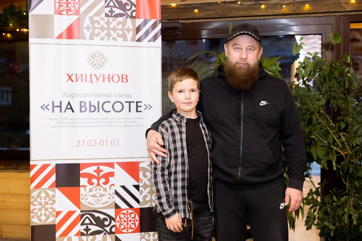 Корпоративный съезд «Хицунов» «На высоте» в Архызе: участник с сыном у баннера бренда